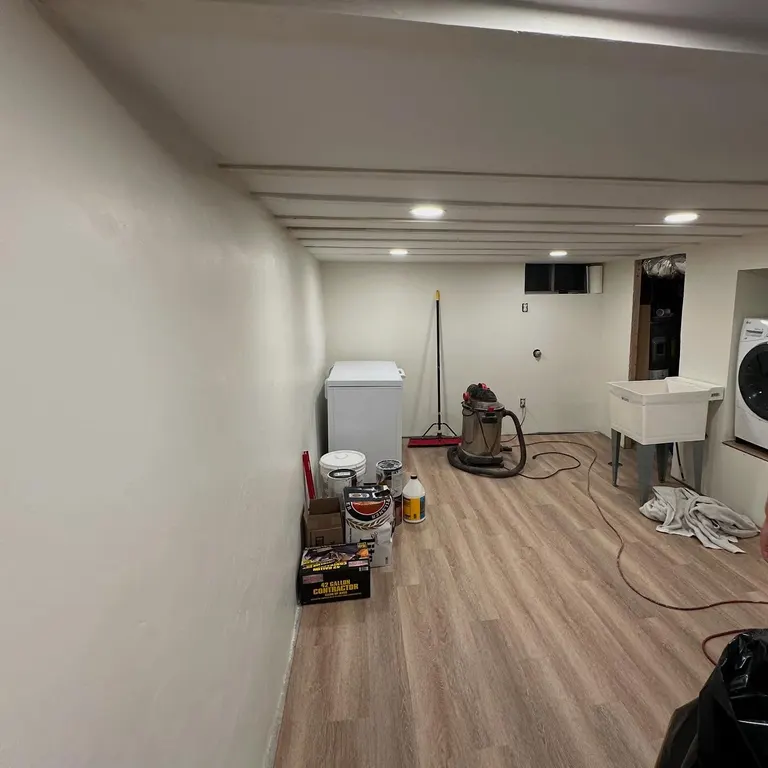 Basement interior with recessed lights, wood-effect floor, neutral walls and some unfinished furnishing.