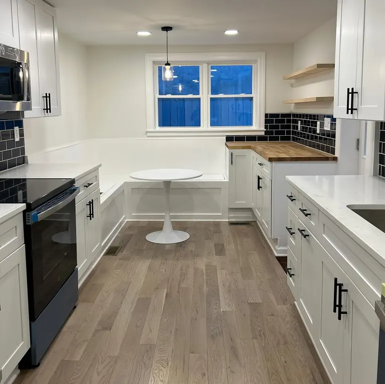 White kitchen with island, white cabinets, wood floor and blue dusk at the rear window.