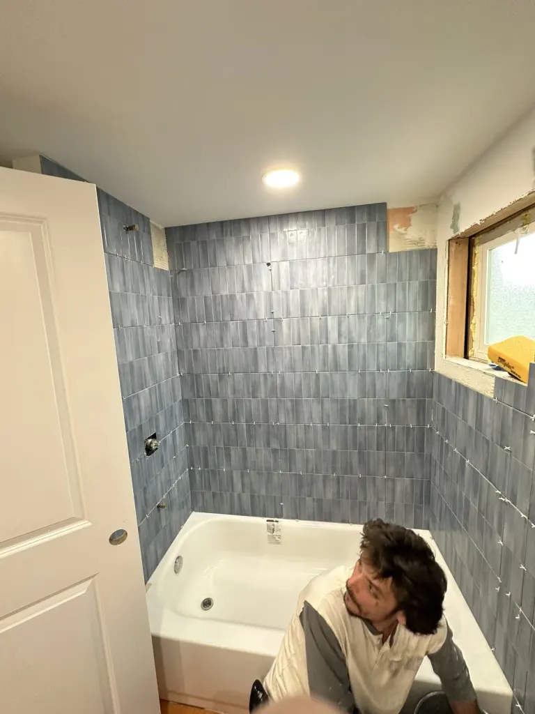 The tub bathroom during construction, with blue wall tile and a worker beside the tub.