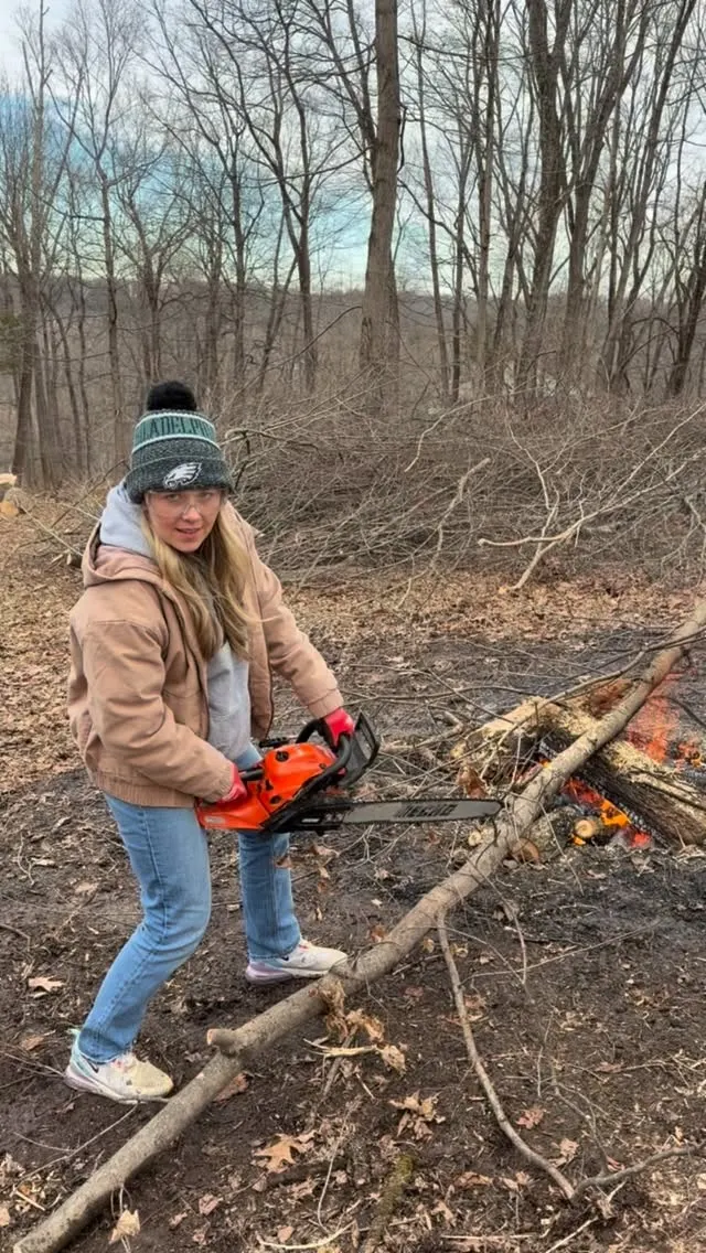 A person holding a chainsaw beside felled trees in winter woodland.